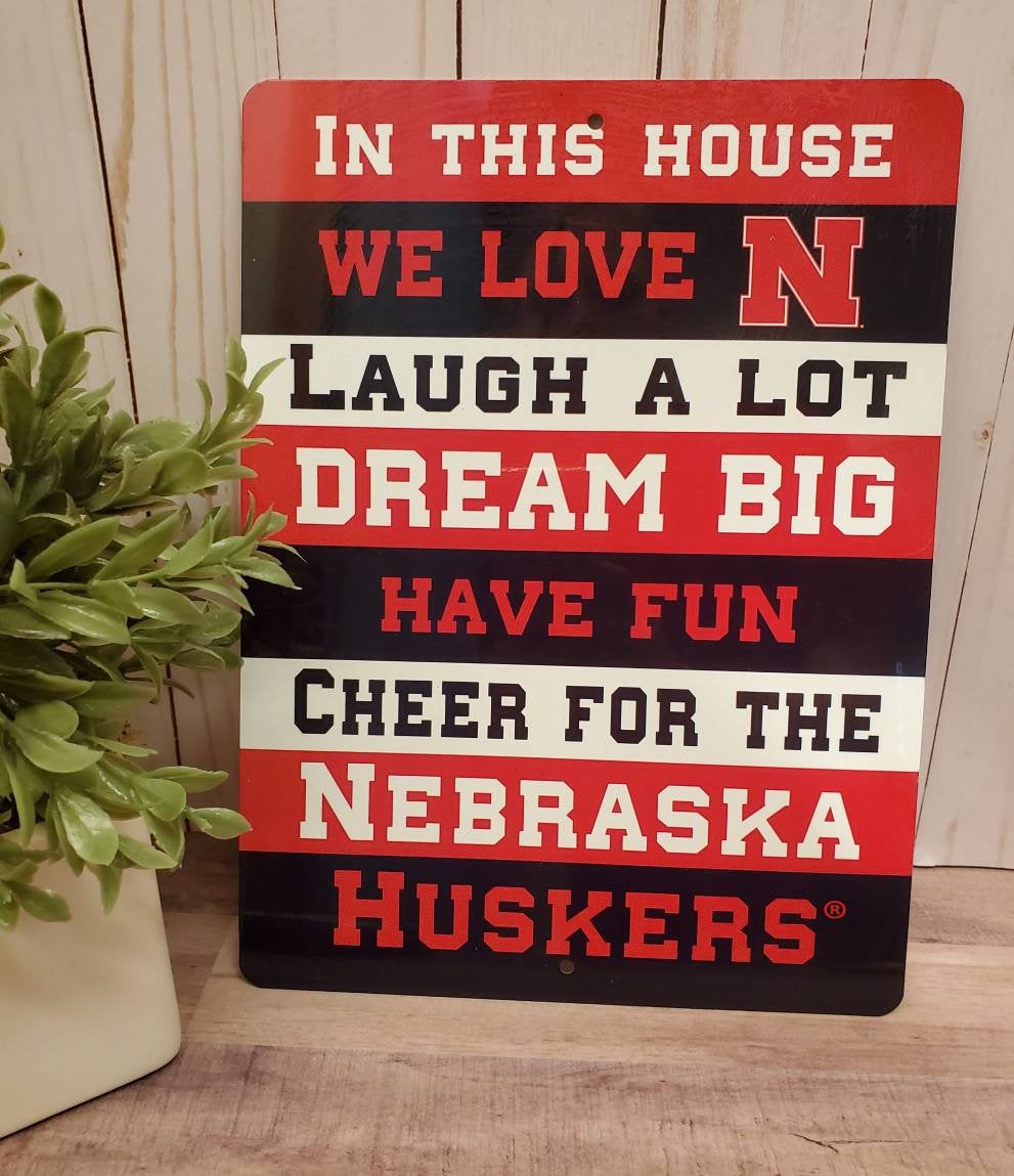 In this house, we love Nebraska, laugh a lot, dream big, have fun, and cheer for the Nebraska Huskers metal sign
